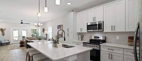 A modern kitchen with white cabinets, a large island with bar stools, stainless steel appliances, and pendant lighting.