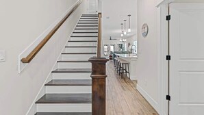 Eine Treppe mit Holzhandläufen und einer Holzsäule, die zu einem Küchenbereich mit einer Bar und Hockern führt.
