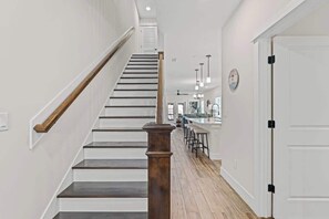 Eine Treppe mit Holzhandläufen und einer Holzsäule, die zu einem Küchenbereich mit einer Bar und Hockern führt.