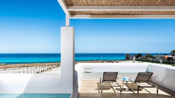 Un balcón con vista al mar, dos sillas y una mesita.