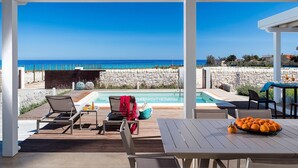 Un espacio al aire libre cubierto con piscina, sillones de descanso y una mesa con fruta.