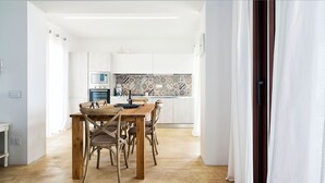Una cocina moderna con armarios blancos, salpicadero con diseño y un comedor con sillas de madera y una mesa.