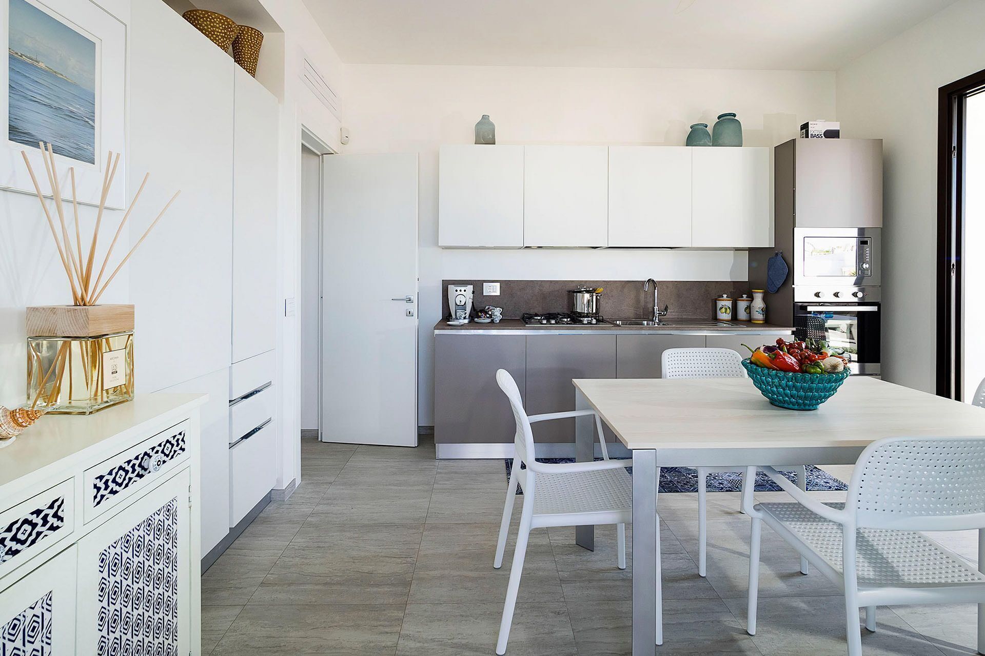 Une cuisine moderne avec des meubles blancs, une table à manger avec des chaises et un îlot de cuisine sur lequel se trouve un saladier rempli de fruits.