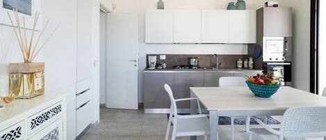 Une cuisine moderne avec des meubles blancs, une table à manger avec des chaises et un îlot de cuisine sur lequel se trouve un saladier rempli de fruits.