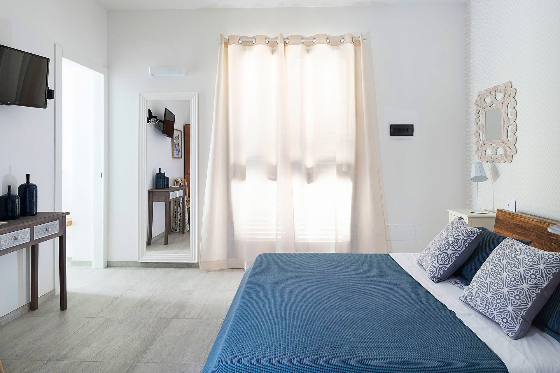 A bedroom with a bed, a desk, and a mirror.