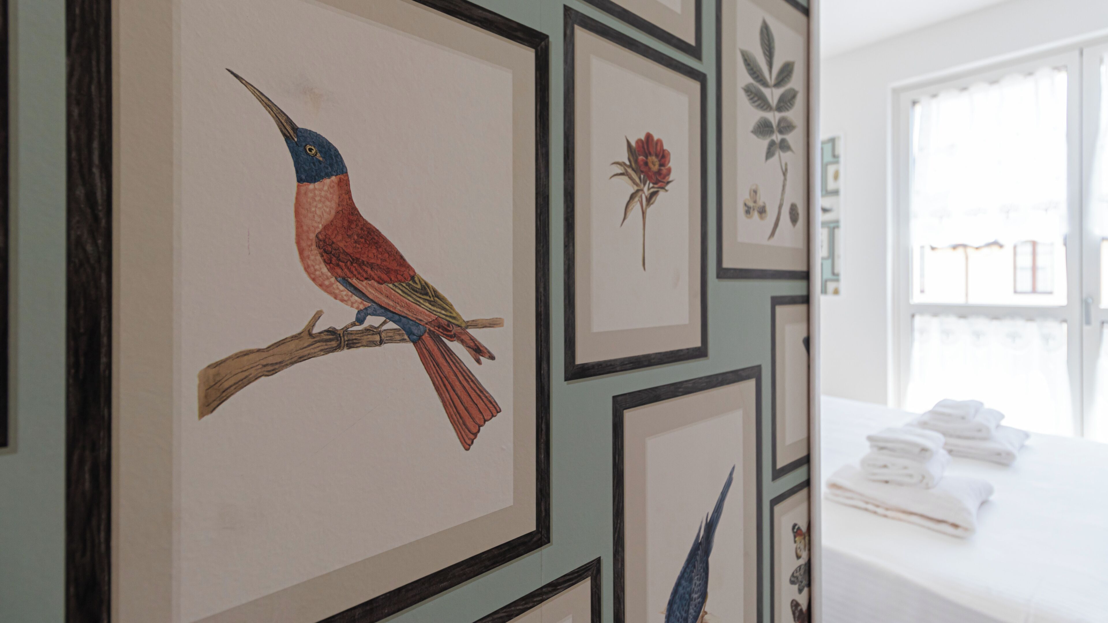 A room with framed artwork on the wall, a window with curtains, and a table with folded towels.