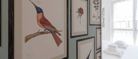 A room with framed artwork on the wall, a window with curtains, and a table with folded towels.