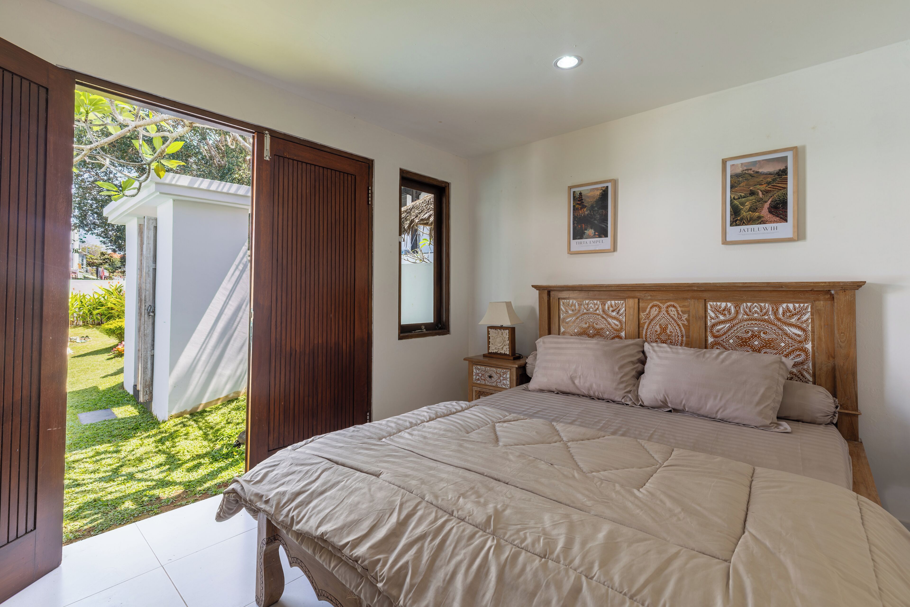 Een slaapkamer met een groot bed, een houten hoofdeinde en uitzicht op een tuin door een open deur.
