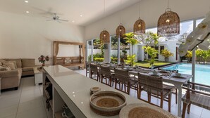 Un vaste espace de vie comprenant une grande table à manger, des chaises en osier et un ventilateur de plafond.