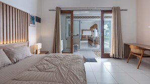 Une chambre à coucher avec un grand lit, un bureau, une chaise et une salle de bain visible à travers une porte ouverte.