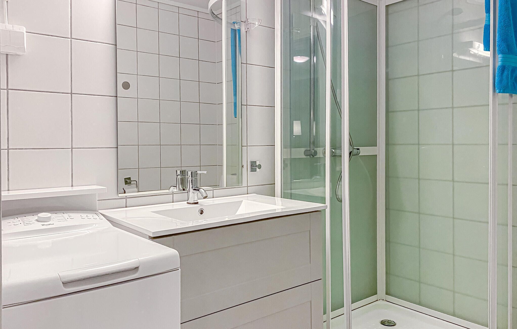 A modern bathroom with a white sink, a mirror, and a glass-enclosed shower.