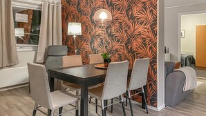 A dining area with a dark wooden table, six chairs, and a wall with a tropical leaf pattern.