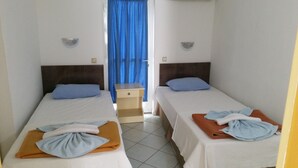 A hotel room with two single beds, each with a blue pillow and a folded towel. There is a small bedside table between the beds, and the room has a tiled floor. - Özlem  1 Apart (Marmaris)