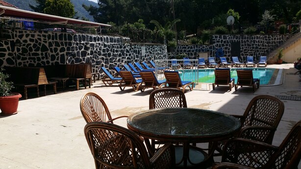 A poolside area with lounge chairs and a table, surrounded by stone walls and potted plants. - Özlem  1 Apart (Marmaris)