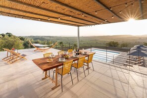 A terrace with a wooden table set for dining, a hammock, and a pool. - Villa Arcobaleno with pool - My Rental Homes (Noto)