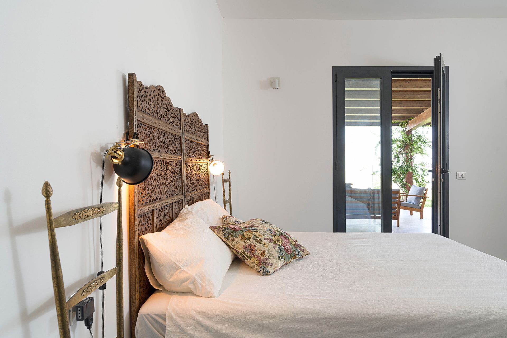 A bedroom with a wooden headboard, a bed with a floral pillow, and a nightstand with a lamp.