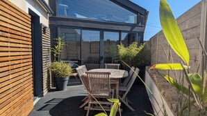 A modern outdoor patio with a wooden table and chairs, surrounded by potted plants and a wooden fence. - L'Abri de la Plage, L'Abri de la plage - Maison de bord de mer en Bretagne (Lampaul-Plouarzel)