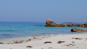A beach with clear blue water, large rocks, and seaweed on the sand. - L'Abri de la Plage, L'Abri de la plage - Maison de bord de mer en Bretagne (Lampaul-Plouarzel)