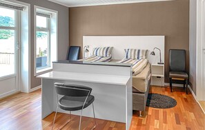 Une chambre à coucher de taille modeste, comprenant un lit, un bureau et une chaise, une petite table de chevet et une vue par la fenêtre.