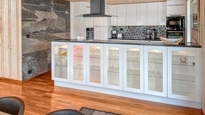 A modern kitchen with a marble backsplash, white cabinetry, and a central island with glass-fronted cabinets displaying wine glasses. - 5 bedroom awesome home in Eidsvåg i Romsdal (Eidsvåg i Romsdal)