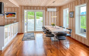Une cuisine moderne avec un lambris en bois, une grande table à manger entourée de chaises et une vue sur l’extérieur grâce à des portes vitrées.