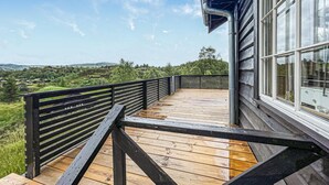 En træterrasse med gelænder i sort, med udsigt over et grønt landskab med huse i det fjerne.