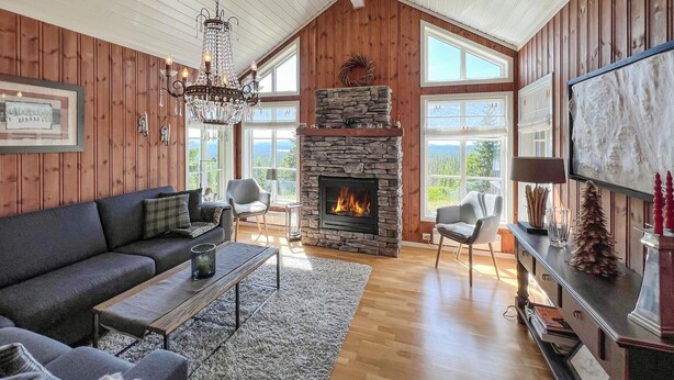 Un salon chaleureux avec une cheminée en pierre, des murs en bois et une grande fenêtre donnant sur l’extérieur.