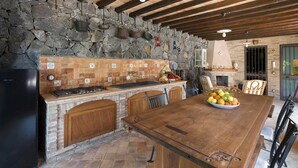 Una cucina rustica con parete in pietra, pensili in legno, un grande tavolo in legno e un piano cottura integrato.