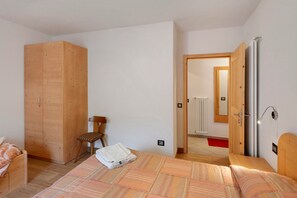 Un dormitorio con cama, un armario de madera, una silla y una puerta que da a otra habitación.