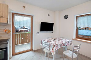 Un comedor con una mesa preparada para cuatro personas, un televisor montado en la pared y una ventana con vistas a edificios.
