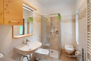 Un baño con cabina de ducha de vidrio, lavamanos, bidé e inodoro.