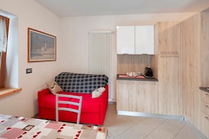 Un ambiente abitativo compatto con un divano rosso, un angolo cottura e un quadro appeso al muro.
