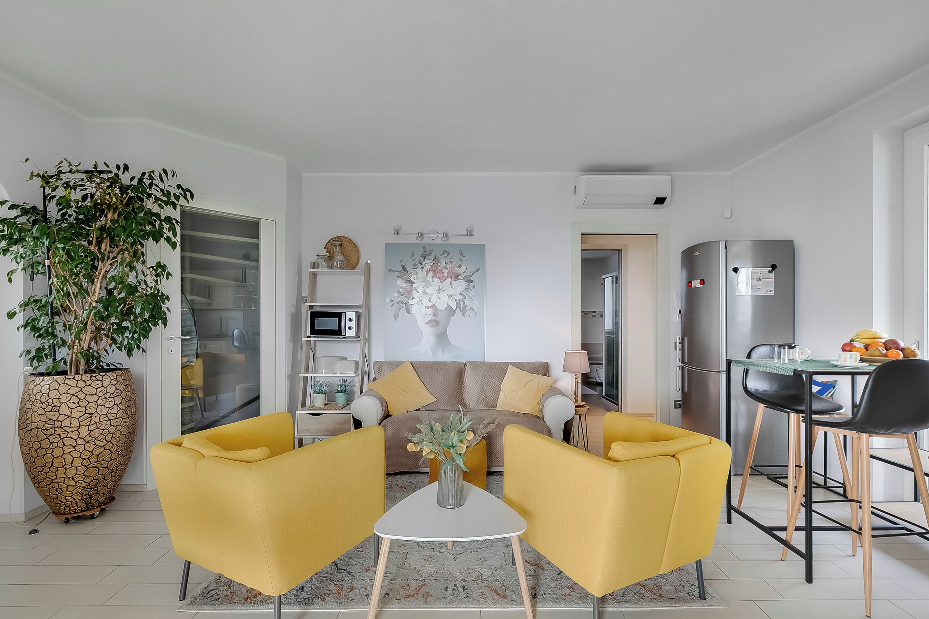 Un salon moderne avec un canapé, des fauteuils jaunes, une table basse et une grande plante en pot.