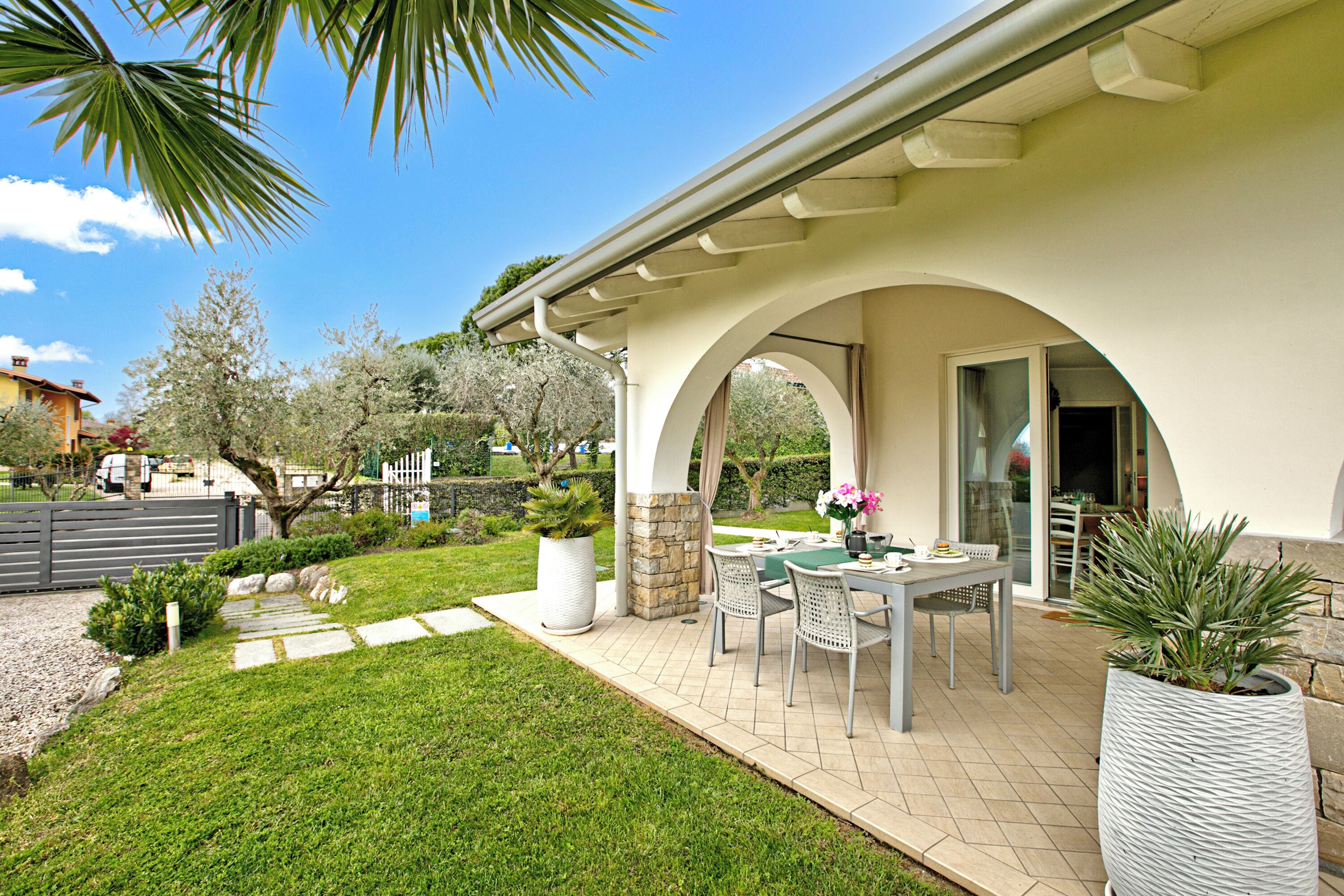A patio with a table and chairs, surrounded by a well-maintained lawn and potted plants.