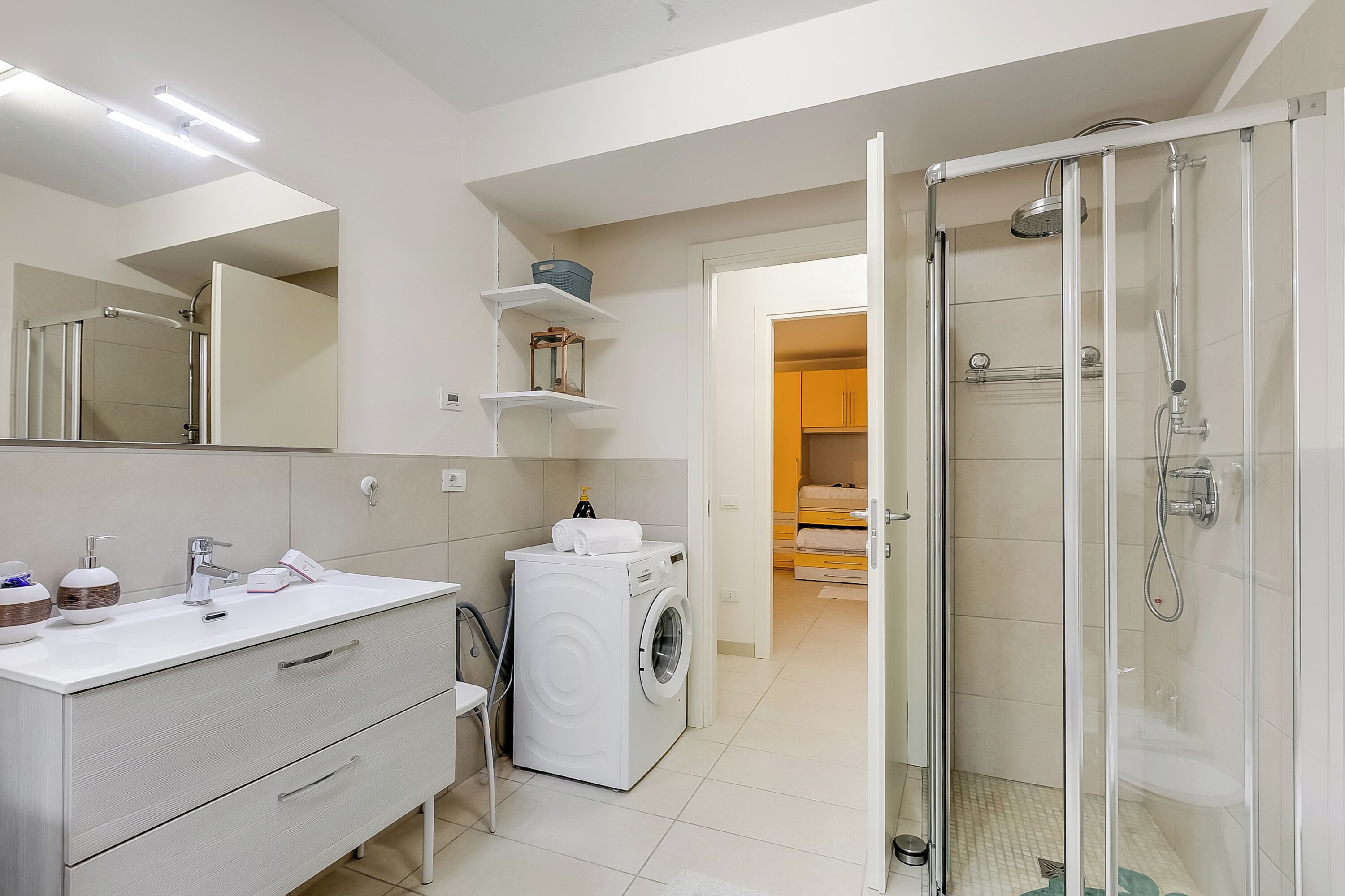 Un baño moderno con lavamanos blanco, espejo y ducha con mampara de vidrio.