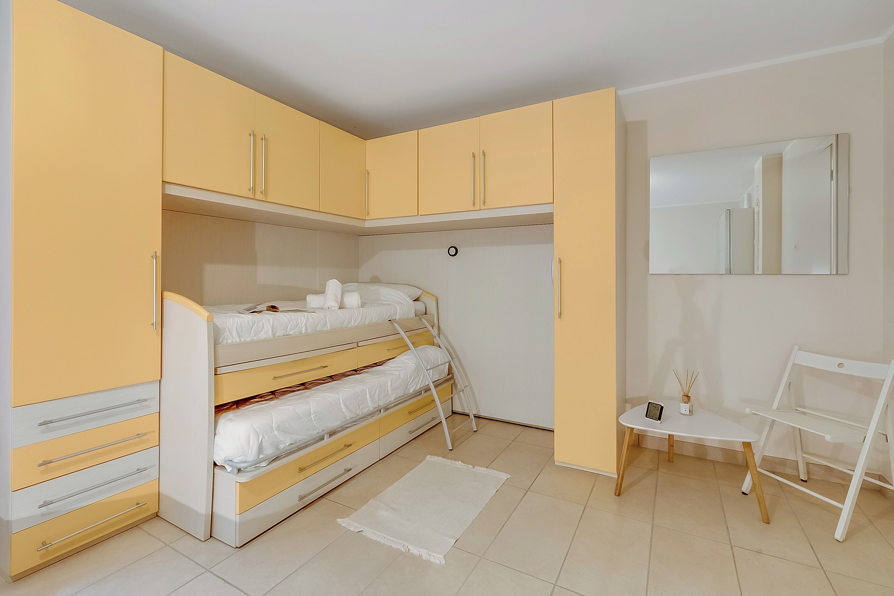 A bedroom with a bunk bed, a desk with a chair, and a mirror on the wall.