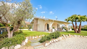 A modern house with a covered patio, stone walls, and a well-maintained lawn. - Il Silenzio House- Manerba del Garda Villa With Garden (Manerba del Garda)