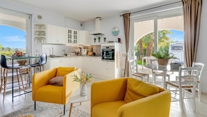 A modern kitchen with white cabinets, a dining area with yellow chairs, and a view of palm trees. - Il Silenzio House- Manerba del Garda Villa With Garden (Manerba del Garda)