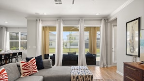 A modern living room with a sectional sofa, ottomans, a dining area, and large windows with curtains. - Luxury 5bed Villa with Complimentary Pool Heating (Kissimmee)