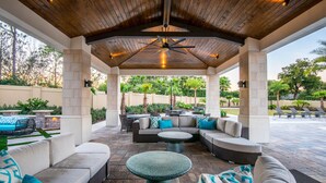 A covered outdoor patio with seating areas, a ceiling fan, and a view of the surrounding greenery. - Luxury 5bed Villa with Complimentary Pool Heating (Kissimmee)