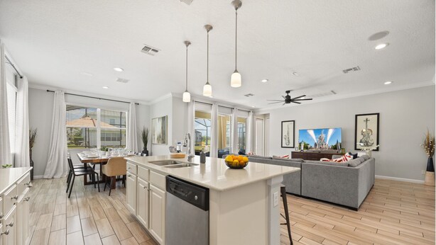 A modern kitchen with a central island, a dining area with a table and chairs, and a living area with a sofa and TV. - Luxury 5bed Villa with Complimentary Pool Heating (Kissimmee)