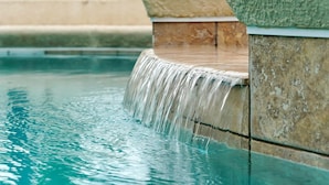 A pool with a stone ledge and a waterfall feature. - Luxury 5bed Villa with Complimentary Pool Heating (Kissimmee)