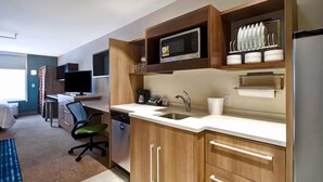 A modern kitchen with wooden cabinets, a microwave, a sink, and a dishwasher. There is a dining area with a table and chairs, and a television in the background. - Roomy Suite for a Relaxing Stay – Close to Exciting Wichita Spots (Wichita)