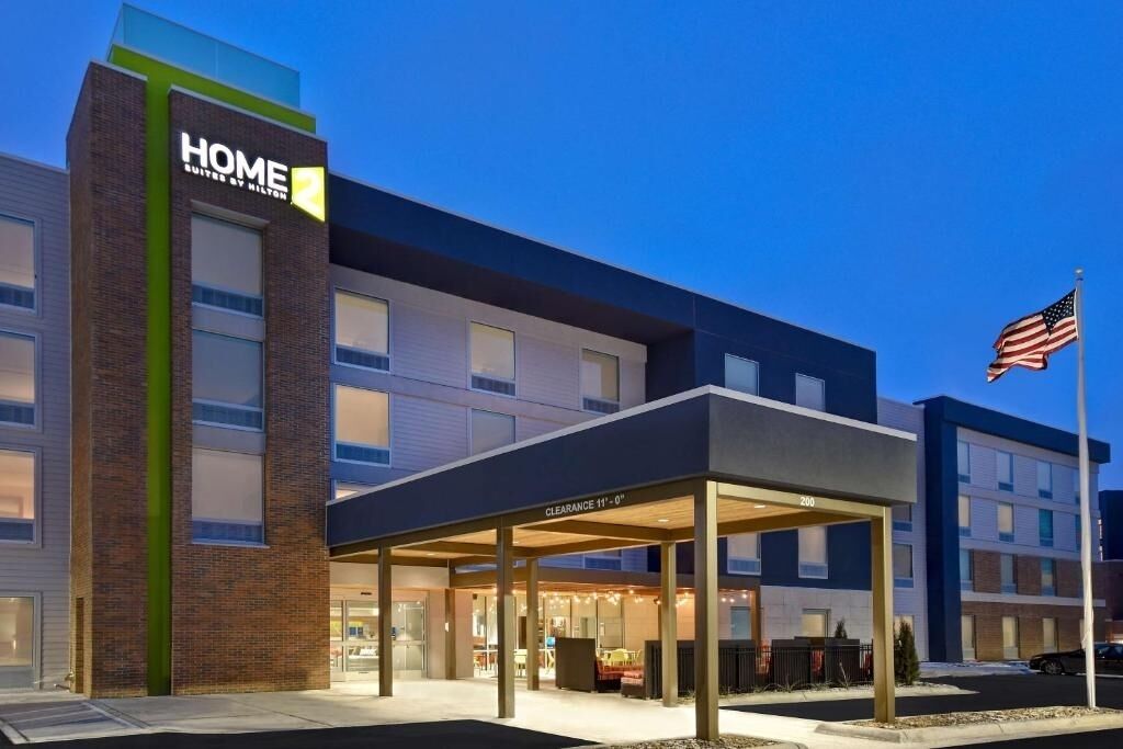 A modern hotel with a clear entrance, a covered waiting area, and an American flag.
