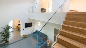 A modern interior with a glass staircase, a blue sofa, and a flat-screen TV. - Villa Cloris sea view and pool - My Rental Homes (Mascali)