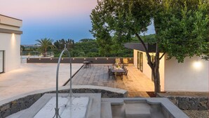 A rooftop patio with a stone fire feature, outdoor seating, and a view of the cityscape. - Villa Cloris sea view and pool - My Rental Homes (Mascali)