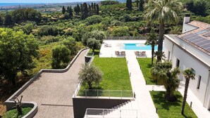 A modern villa with a swimming pool, surrounded by lush greenery and a view of the cityscape. - Villa Cloris sea view and pool - My Rental Homes (Mascali)