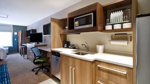 A modern kitchen with wooden cabinets, a microwave, a sink, and a dishwasher. There is a dining area with a table and chairs, and a television in the background. - Comfortable Suite w/ Ample Breakfast Options Near Local Dining (Wichita)