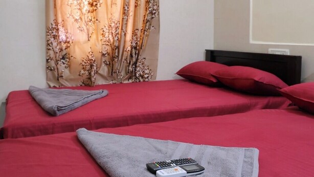 Een hotelkamer met twee bedden, rode beddengoed, een afstandsbediening en een airconditioning aan de muur.