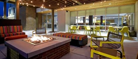 An outdoor seating area with a fire pit, yellow chairs, and a brick fireplace.